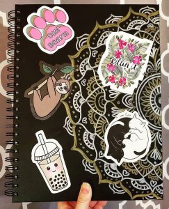 a variety of cute redbubble stickers on a black notebook